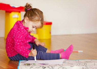 İki-yıl-yaşlı kız çizer ve evde yerde renk.