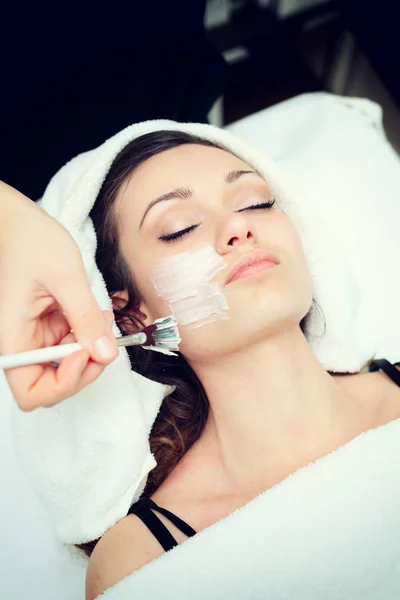 Cosmetician applying facial beauty mask for young beautiful woman at spa salon