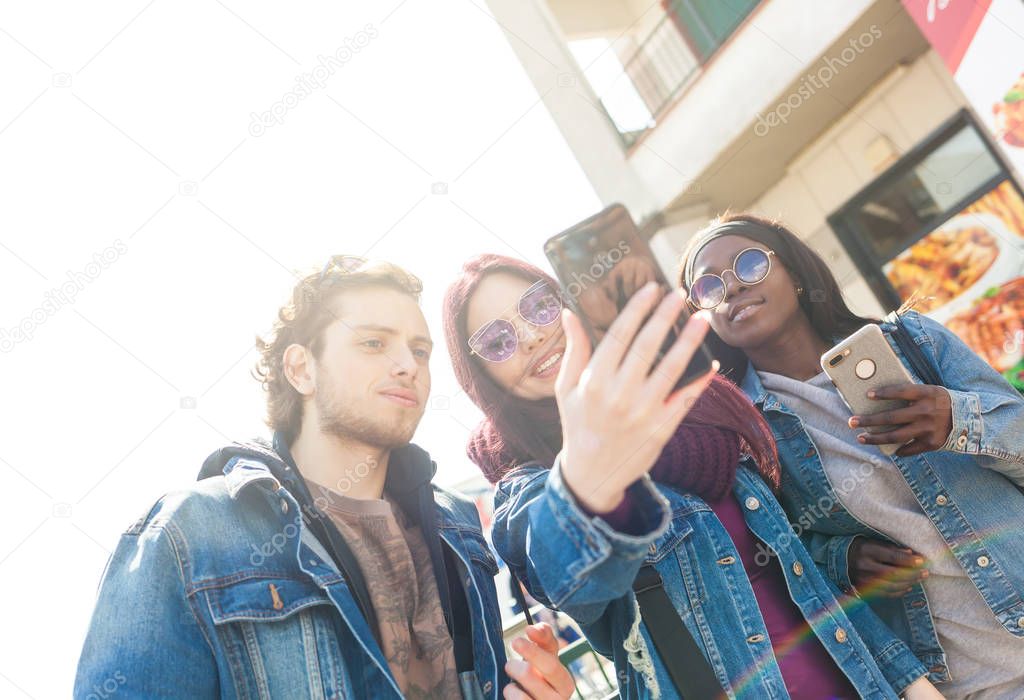 Multiracial friends taking selfie outdoors.