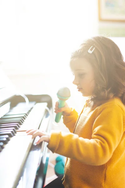 Girl toddler plays with piano and toy microphone. — Stock Photo, Image