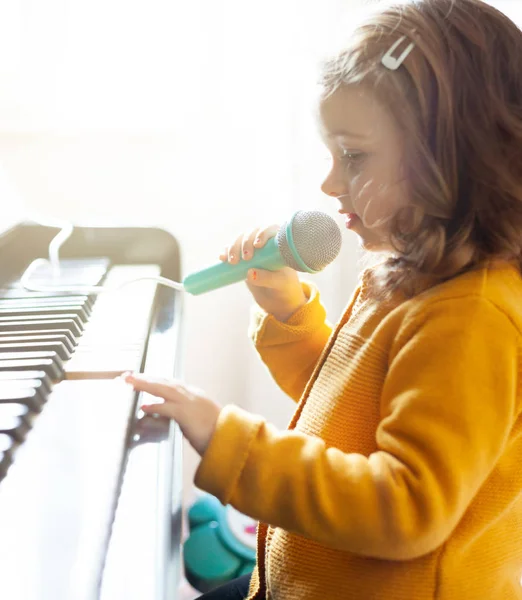 Girl toddler plays with piano and toy microphone. — Stock Photo, Image