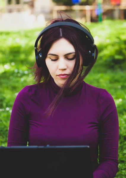 Young woman in park using laptop computer listening music. — Stock Photo, Image