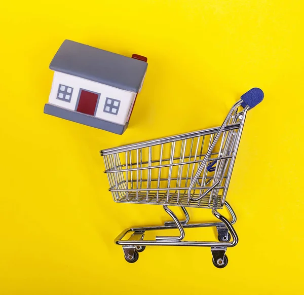 Shoping cart met rubberen huizen op een gele achtergrond. — Stockfoto