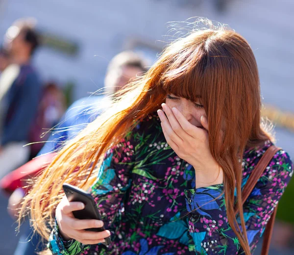 Young woman laughs looking at mobile phone. — Stock Photo, Image