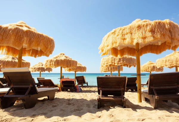 Strand schöne reetgedeckte Sonnenschirme und türkisfarbenes Meer. — Stockfoto
