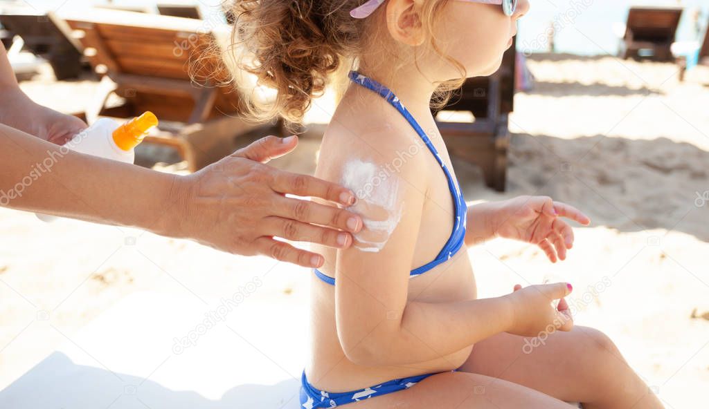 Mom puts sunscreen on the shoulders of her daughter.