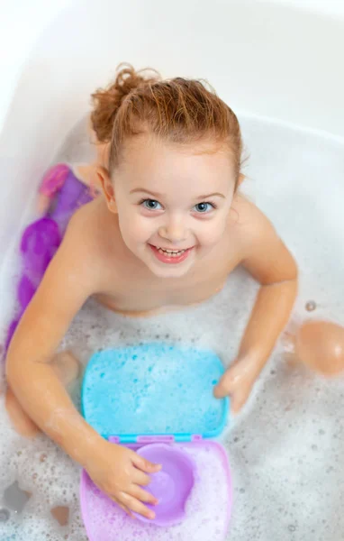 Девочка принимает ванну и играет с пластиковыми игрушками — стоковое фото