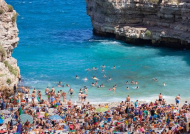 Polignano a Mare, İtalya - 15 Ağustos 2014: İnsanlar güzel Lama Monachile plajında rahatlar ve yüzerler. Kayalık duvarlar arasına kurulmuş beyaz çakıl taşı koy ve kristal berrak deniz mağaralarıyla yıkanmış..