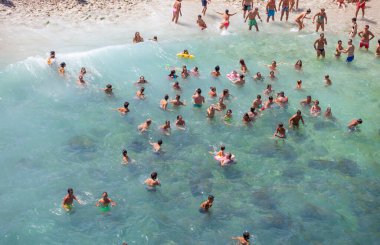 Polignano a Mare, İtalya - 15 Ağustos 2014: İnsanlar güzel Lama Monachile plajında rahatlar ve yüzerler. Kayalık duvarlar arasına kurulmuş beyaz çakıl taşı koy ve kristal berrak deniz mağaralarıyla yıkanmış..