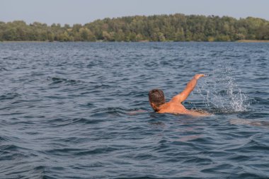 Genç adam bir güneşli ve sıcak günde hızlı gölde yüzüyor