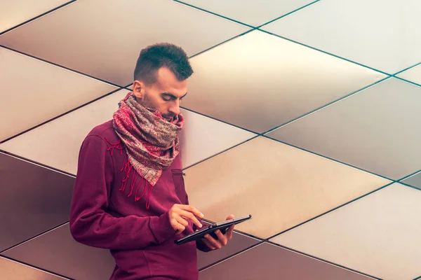 Smart young man works on tablet computer outdoors in urban public space. Millennial using tablet pc with cityscape in background.