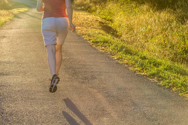 Athletic woman running at a countryside trail in sunrise light. Beautiful female running outside in leafy and green suburb.