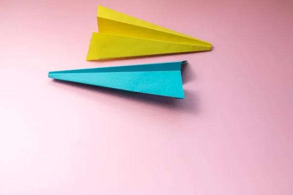 Pastel pembe Kağıt arka planda mavi ve sarı kağıt uçaklar, kopya alanı için yer