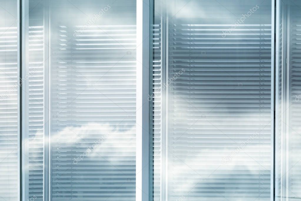 View of louvers window of modern office building with reflection of sky with clouds, blurred effect