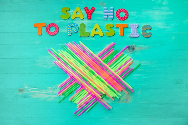 Say no to plastic - colorful wooden letters phrase on green wooden background with plastic straws, top view