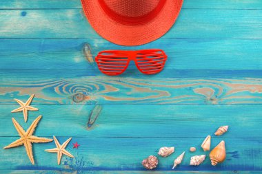 Canlı mercan renkli şapka, panjurlu güneş gözlüğü, deniz kabukları ve denizyıldızı mavi boyalı vintage ahşap doku üzerinde üst görünümü. Düz döşeme, kopyalama alanı.