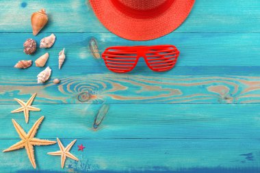 Canlı mercan renkli şapka, panjurlu güneş gözlüğü, deniz kabukları ve denizyıldızı mavi boyalı vintage ahşap doku üzerinde üst görünümü. Düz döşeme, kopyalama alanı.