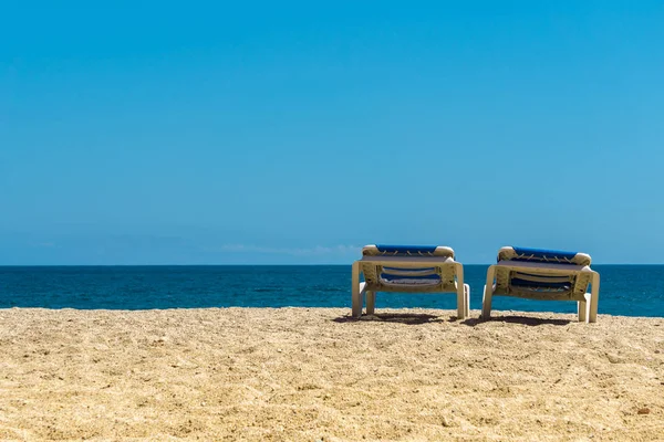 Przybrzeżne krajobrazy, dwa leżaki na piaszczystej plaży na turkusowym morzu i błękitne niebo tle — Zdjęcie stockowe