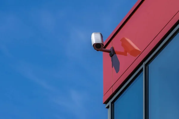 Cámara CCTV en edificio moderno. Cámara de seguridad en la pared roja, fondo azul cielo. Copiar espacio . — Foto de Stock