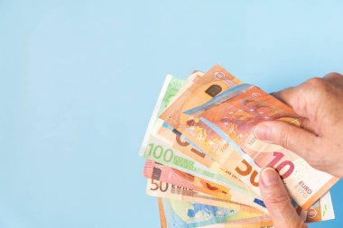 Mavi arka planda Avrupa banknotlarını tutan eller. Gök mavisi arka planda avro banknotları olan eller. Fotokopi alanı ile arka planda farklı değerlerin Euro parası