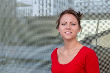 Şehrin arka planında kameraya bakan neşeli bir kadın. Şehir zemininde bir kadın. Neşeli kadın portresi. Gülümseyen bayana yakın durun. Başarılı kadın konsepti.