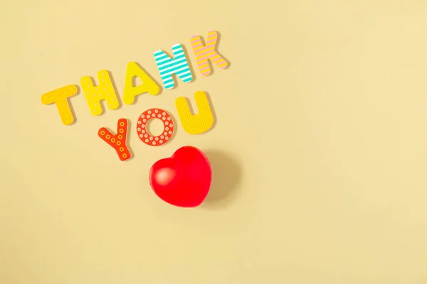 Thank you words and red heart isolated on background. Red heart and text THANK YOU of colorful wood letters on yellow backdrop. Appreciation to medical staff. Thanks to doctors and nurses in hospitals