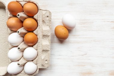 Geri dönüşümlü karton kutuda kahverengi ve beyaz yumurtalar ve ahşap masanın yanında iki tavuk yumurtası. Karton kutuda serbest organik yumurta. Ahşap arka planda yumurtaları olan bir kutu. Üst görünüm, alanı kopyala