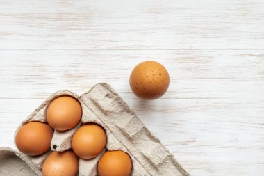 Karton kutuda serbest organik yumurtalar. Yakın plan kahverengi yumurtalar geri dönüşümlü karton kutuda ve bir tane de ahşap arka planda. Tahta masanın üzerinde kahverengi tavuk yumurtaları olan bir kutu. Üst görünüm, alanı kopyala.