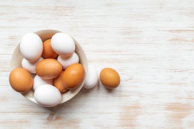 Tabakta kahverengi ve beyaz yumurta ve ahşap arka planda da iki yumurta. Kasede organik yumurta var. Tahta masanın üzerinde kahverengi ve beyaz tavuk yumurtaları olan bir kase. Üst görünüm, boşluğu kopyala. Doğal sağlıklı yiyecekler.