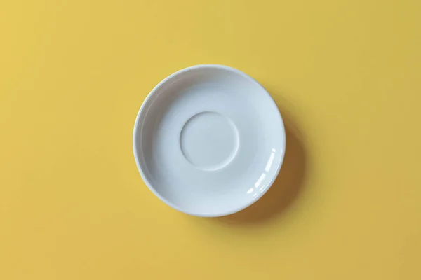 Sarı arka plana yerleştirilmiş pasta için beyaz tabak. Sarı arka planda izole edilmiş boş seramik yuvarlak tabak. Düz yatıyordu. Üst görünüm.