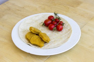 Pişmiş tavuk nuggets ve küçük kırmızı taze domates bir kahvaltı geniş beyaz tabakta Merkezi'nde ince ekmek ile perspektif çekim