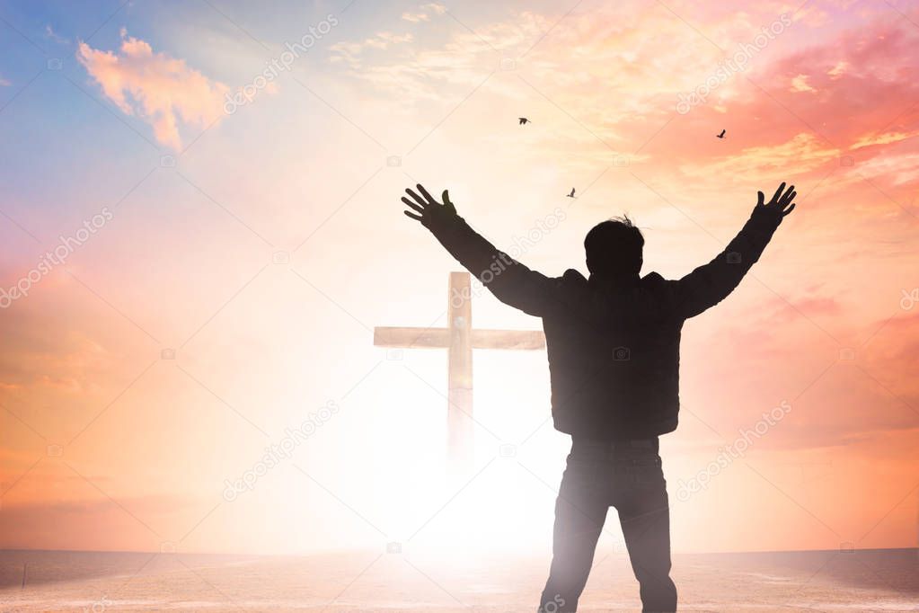 Emotional wellness concept: Silhouette of man raised hands at sunset meadow background