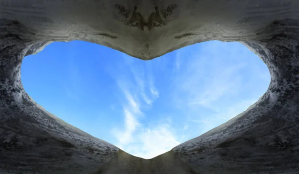 World Heart Day concept: heart shaped cave in the background of blue sky with clouds