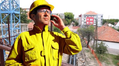 İnşaat işçisi ile sarı kişisel koruyucu ekipman smartphone kullanarak site oluşturma