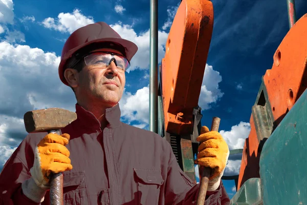 石油工人拿着大锤在泵千斤顶油井前对多云的蓝天背景 — 图库照片