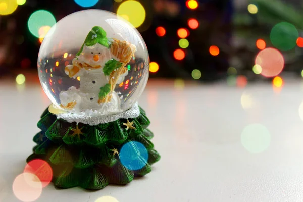 Christmas toy Snowman in a ball on a light background, a sprig of spruce. Free space for text