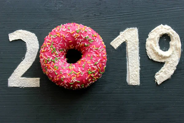 Siyah bir arka plan üzerinde rakamlar 2019 un, pembe çörek numarası 0, yeni yıl, tatlı hayat kavramı yerine dolu. Metin için boş alan