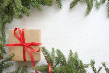 Çerçeve beyaz ahşap zemin üzerine yeşil çam dalları, hediye kutusu ile kırmızı saten kurdele, Noel kartı. Alan üst görünüm Kopyala