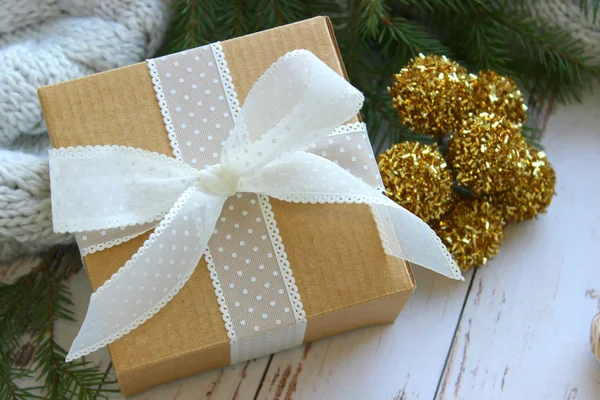 Close - up of a gift box with a white ribbon on a wooden textured white background surrounded by green spruce branches. New year, Christmas background. Copy space
