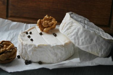 Camembert peyniri yakın çekim. Arka plan ağaç beyaz kağıt üzerinde yuvarlak Camembert peyniri. Gurme peynir, peynir tabağı, şarap yemek. Camembert peyniri. Taze brie peyniri ve fındık, bir ahşap tahta kesim tatlım ve bırakır. İtalyan, Fransız chee