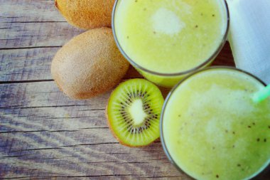 Yaz serinletici bir içecek. Sağlıklı yemek, vejetaryenlik. Ahşap bir masa üzerinde taze kivi dilimleri yanında bir bardak kivi smoothie. meyve içeceği.kopya alanı