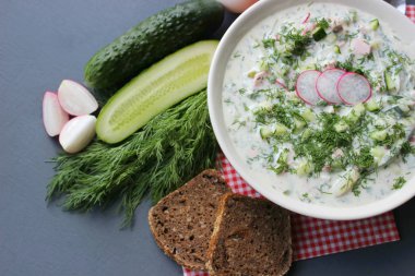 Okroshka seramik bir kase geleneksel bir Rus yaz soğuk çorba. Malzemeler patates, turp, salatalık, dereotu, yumurta, kefir (yoğurt), sosis. Tahta bir masada yazlık yoğurt soğuk çorbası. Seçici odaklama, kopyalama alanı.