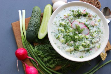 Okroshka seramik bir kase geleneksel bir Rus yaz soğuk çorba. Malzemeler patates, turp, salatalık, dereotu, yumurta, kefir (yoğurt), sosis. Tahta bir masada yazlık yoğurt soğuk çorbası. Seçici odaklama, kopyalama alanı.