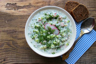 Okroshka seramik bir kase geleneksel bir Rus yaz soğuk çorba. Malzemeler patates, turp, salatalık, dereotu, yumurta, kefir (yoğurt), sosis. Tahta bir masada yazlık yoğurt soğuk çorbası. Seçici odaklama, kopyalama alanı.