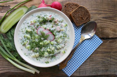 Okroshka seramik bir kase geleneksel bir Rus yaz soğuk çorba. Malzemeler patates, turp, salatalık, dereotu, yumurta, kefir (yoğurt), sosis. Tahta bir masada yazlık yoğurt soğuk çorbası. Seçici odaklama, kopyalama alanı.
