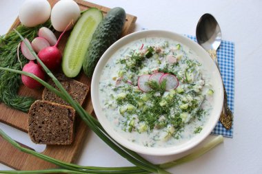 Okroshka seramik bir kase geleneksel bir Rus yaz soğuk çorba. Malzemeler patates, turp, salatalık, dereotu, yumurta, kefir yoğurt, sosis. Tahta bir masada yazlık yoğurt soğuk çorbası. Seçici odaklama, kopyalama alanı.