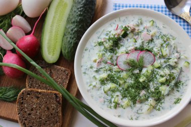 Okroshka seramik bir kase geleneksel bir Rus yaz soğuk çorba. Malzemeler patates, turp, salatalık, dereotu, yumurta, kefir yoğurt, sosis. Tahta bir masada yazlık yoğurt soğuk çorbası. Seçici odaklama, kopyalama alanı.