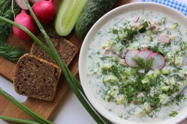 Okroshka seramik bir kase geleneksel bir Rus yaz soğuk çorba. Malzemeler patates, turp, salatalık, dereotu, yumurta, kefir yoğurt, sosis. Tahta bir masada yazlık yoğurt soğuk çorbası. Seçici odaklama, kopyalama alanı.