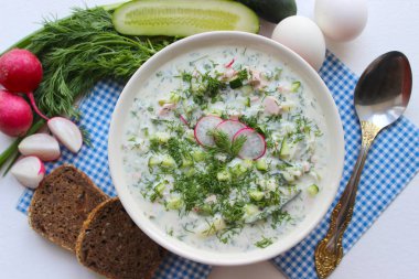 Okroshka seramik bir kase geleneksel bir Rus yaz soğuk çorba. Malzemeler patates, turp, salatalık, dereotu, yumurta, kefir yoğurt, sosis. Tahta bir masada yazlık yoğurt soğuk çorbası. Seçici odaklama, kopyalama alanı.