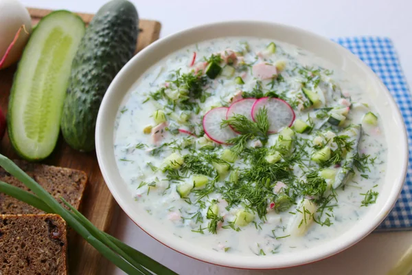 Okroshka seramik bir kase geleneksel bir Rus yaz soğuk çorba. Malzemeler patates, turp, salatalık, dereotu, yumurta, kefir yoğurt, sosis. Tahta bir masada yazlık yoğurt soğuk çorbası. Seçici odaklama, kopyalama alanı.